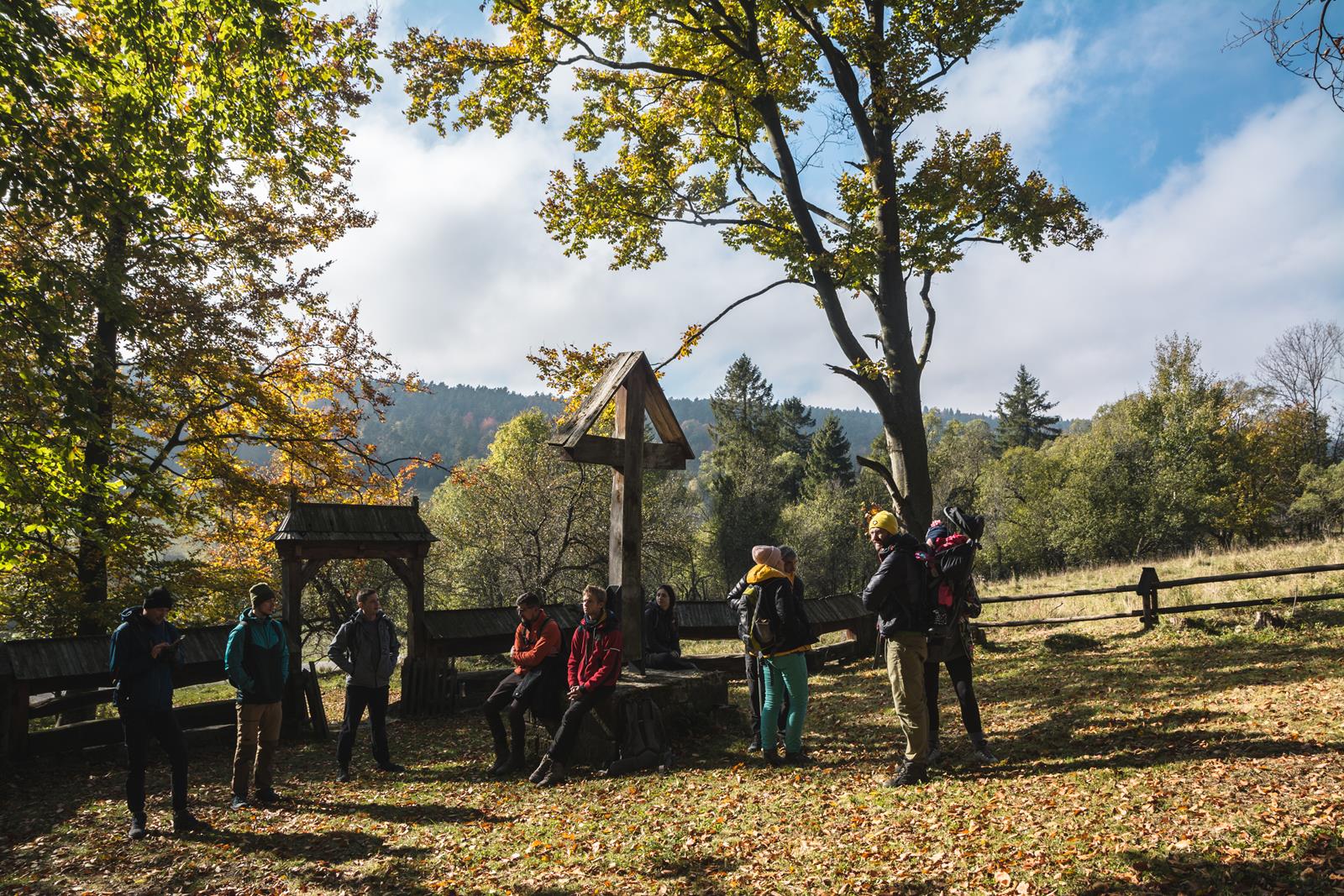 Grupa ludzi w jesiennym krajobrazie stoi przy drewnianym ogrodzeniu cerkwii.