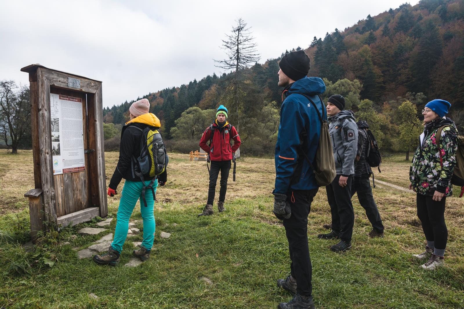 Grupa ludzi ubrana w jesienne stroje wędrówkowe stoi przy pomniku drzwi